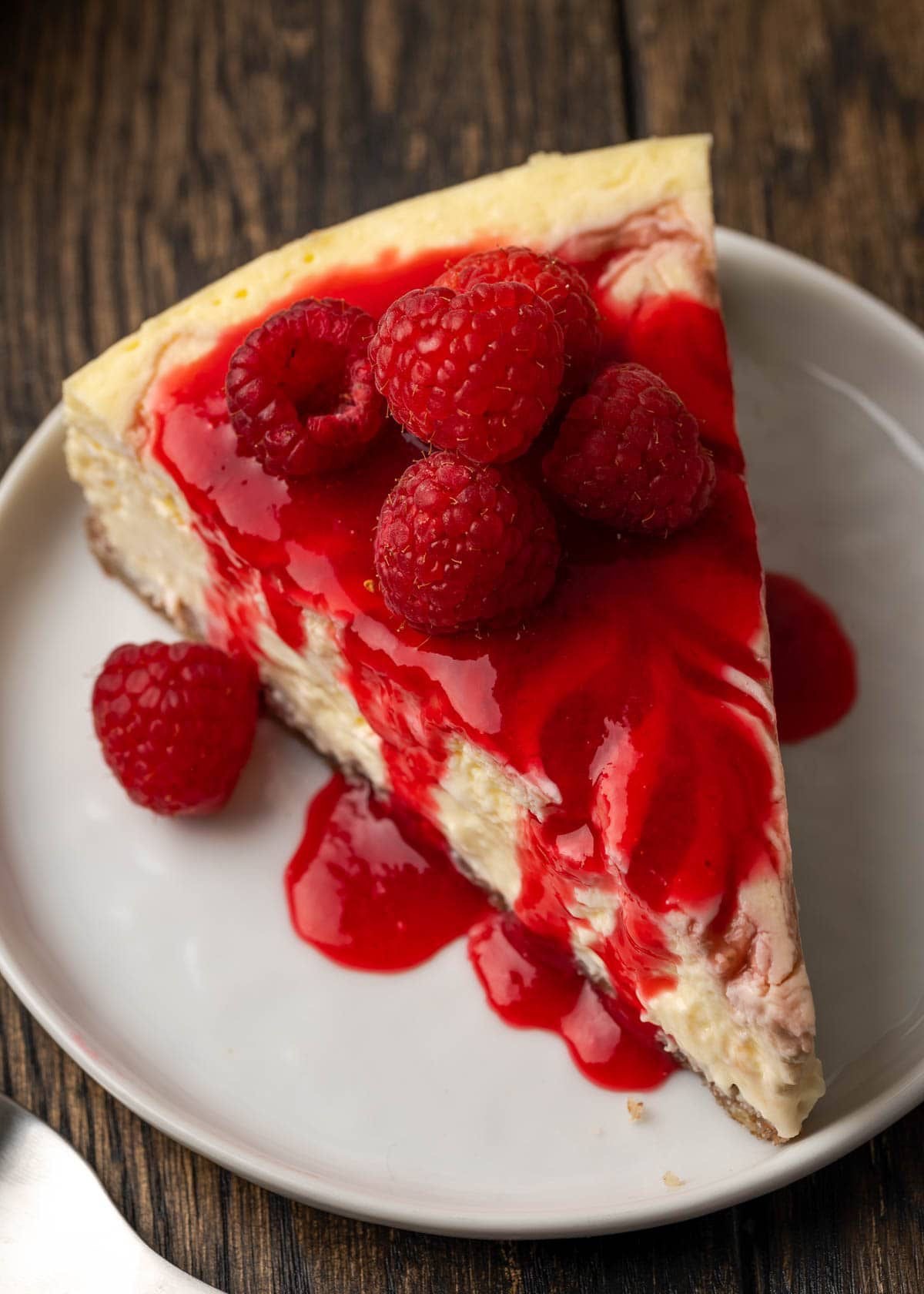 Raspberry Cheesecake — classic slice with fresh raspberry sauce and whole raspberries